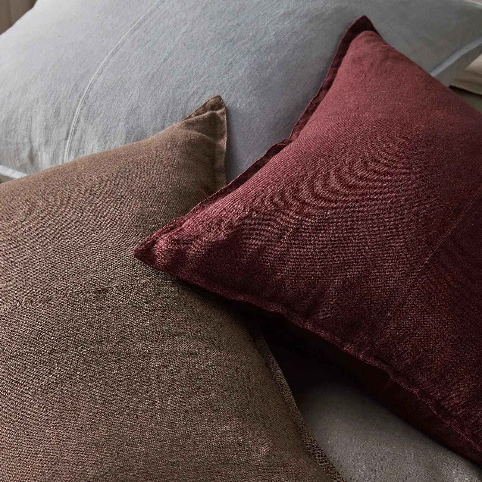 Three textured pillows in brown, red, and gray on a bed.