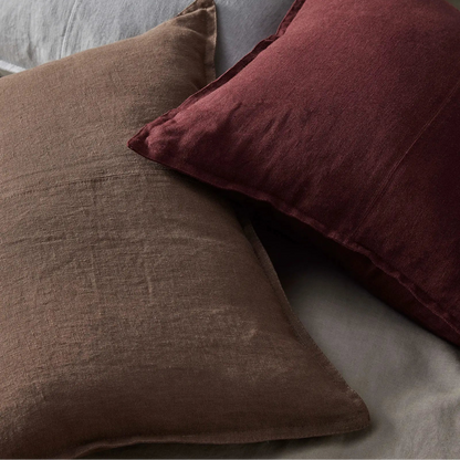 Three textured pillows in brown, red, and gray on a bed.