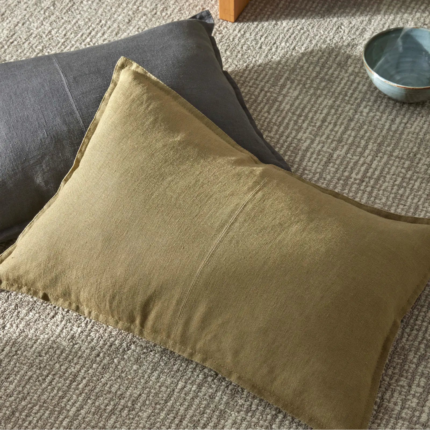 Green cushion on a textured surface with a bowl in the background