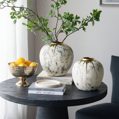 Decorative table setting with ceramic vases, a bowl of fruit, and books against a neutral wall.
