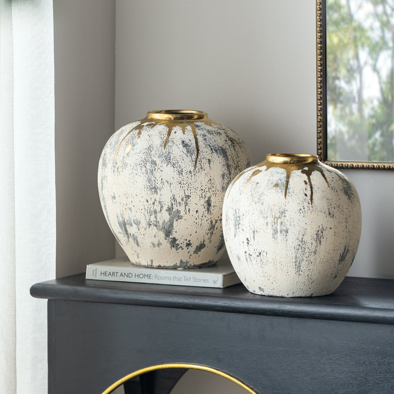 Two decorative ceramic vases on a surface with a mirror and window in the background