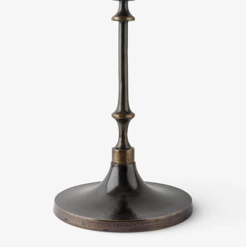 A close-up of a dark bronze metal table lamp base with a flared circular pedestal and a narrow stem, shown against a plain light gray background.
