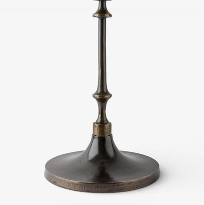 A close-up of a dark bronze metal table lamp base with a flared circular pedestal and a narrow stem, shown against a plain light gray background.