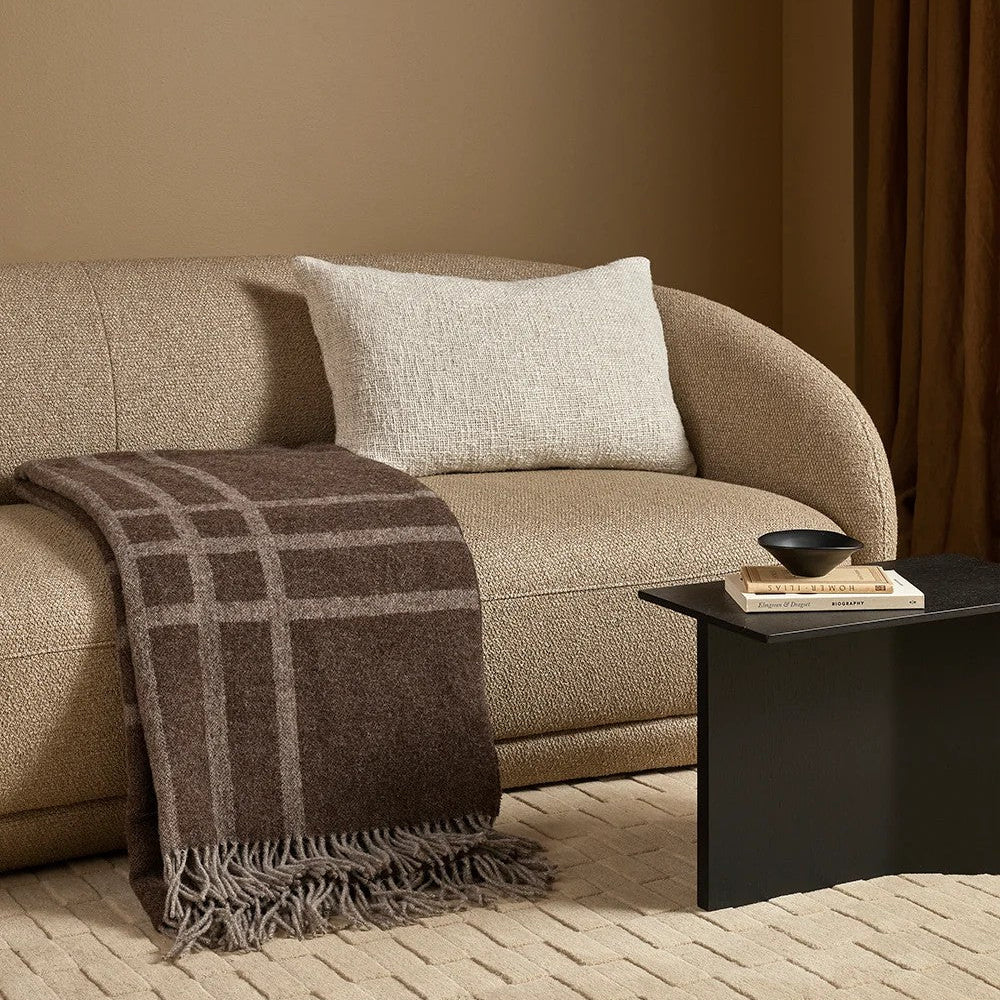Beige sofa with a plaid throw blanket and a side table in a living room setting.
