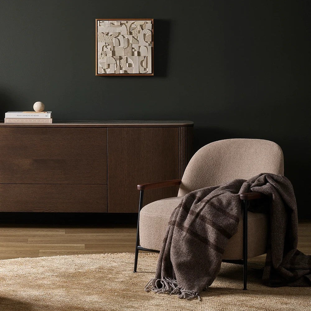 Modern interior with a chair draped with a plaid wool blanket, a cabinet, and a decorative wall piece.