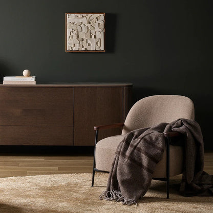 Modern interior with a chair draped with a plaid wool blanket, a cabinet, and a decorative wall piece.