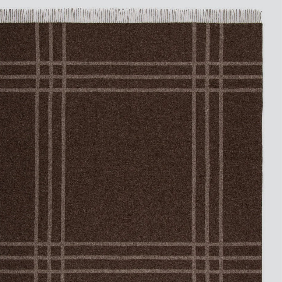 A dark brown woven blanket with a classic plaid pattern in light beige and fringed edges on all sides, shown flat against a white background.