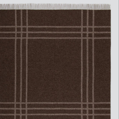 A dark brown woven blanket with a classic plaid pattern in light beige and fringed edges on all sides, shown flat against a white background.