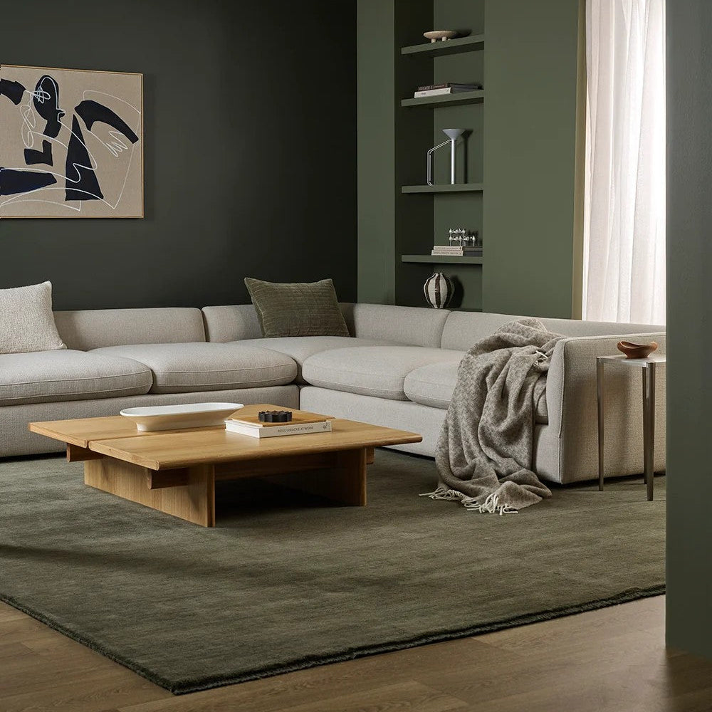 Modern living room with a grey sectional sofa, wooden coffee table, wool throw and bookshelf.