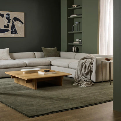 Modern living room with a grey sectional sofa, wooden coffee table, wool throw and bookshelf.