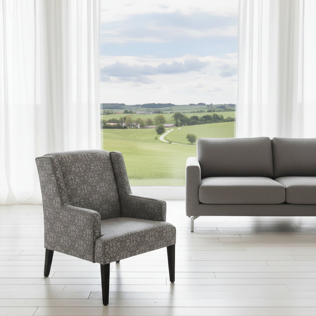 Gray armchair and sofa in a room with large windows showing a view of green fields.