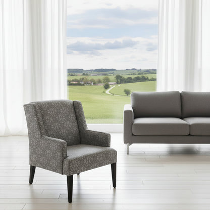 Gray armchair and sofa in a room with large windows showing a view of green fields.