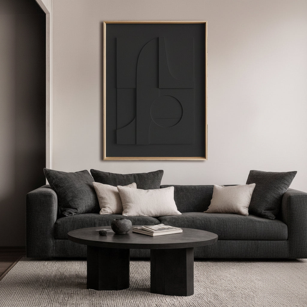 A modern living room scene featuring a large, framed abstract black wall art piece with a thin natural frame hanging above a dark gray sofa with neutral throw pillows.