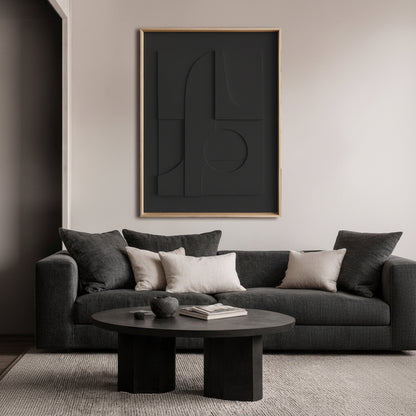 A modern living room scene featuring a large, framed abstract black wall art piece with a thin natural frame hanging above a dark gray sofa with neutral throw pillows.