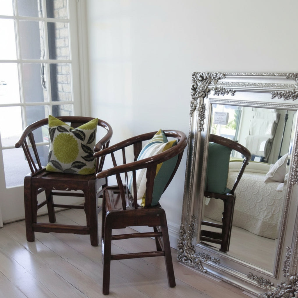 Two wooden chairs with green cushions in front of a large ornate mirror.