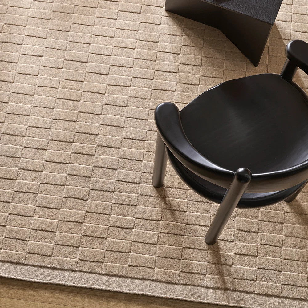 Almond textured rug with a black chair and table in a room setting