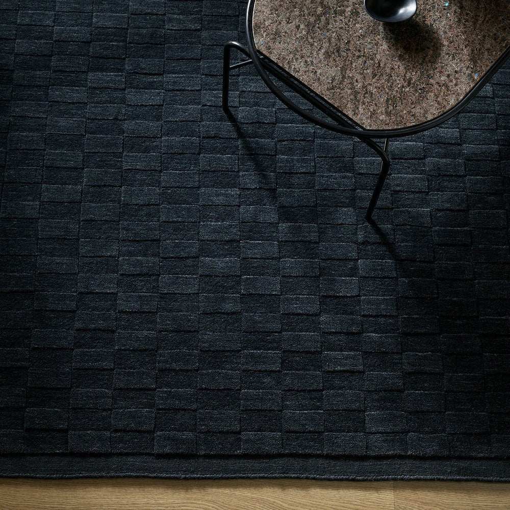 Midnight coloured and textured rug with a modern chair and table on a dark floor.