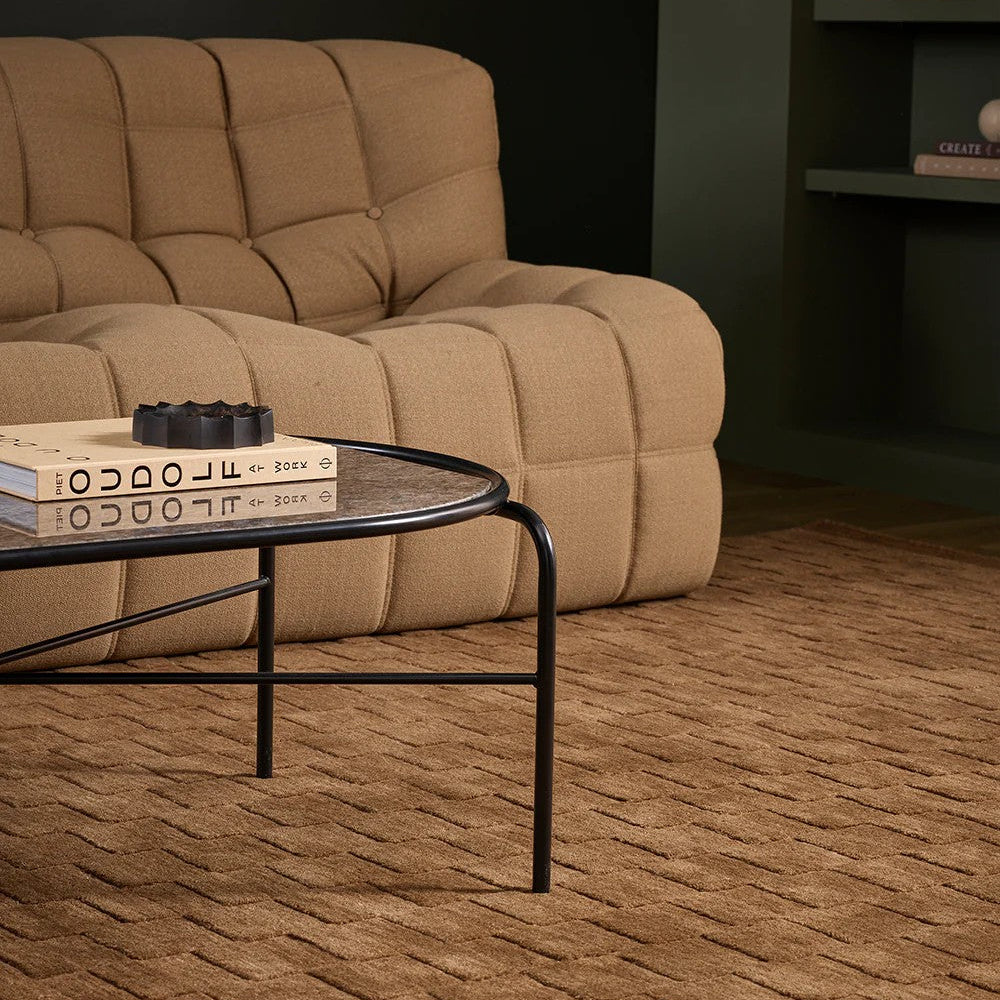 Ginger coloured sofa in a living room with a toffee coloured floor rug, coffee table, and a book.