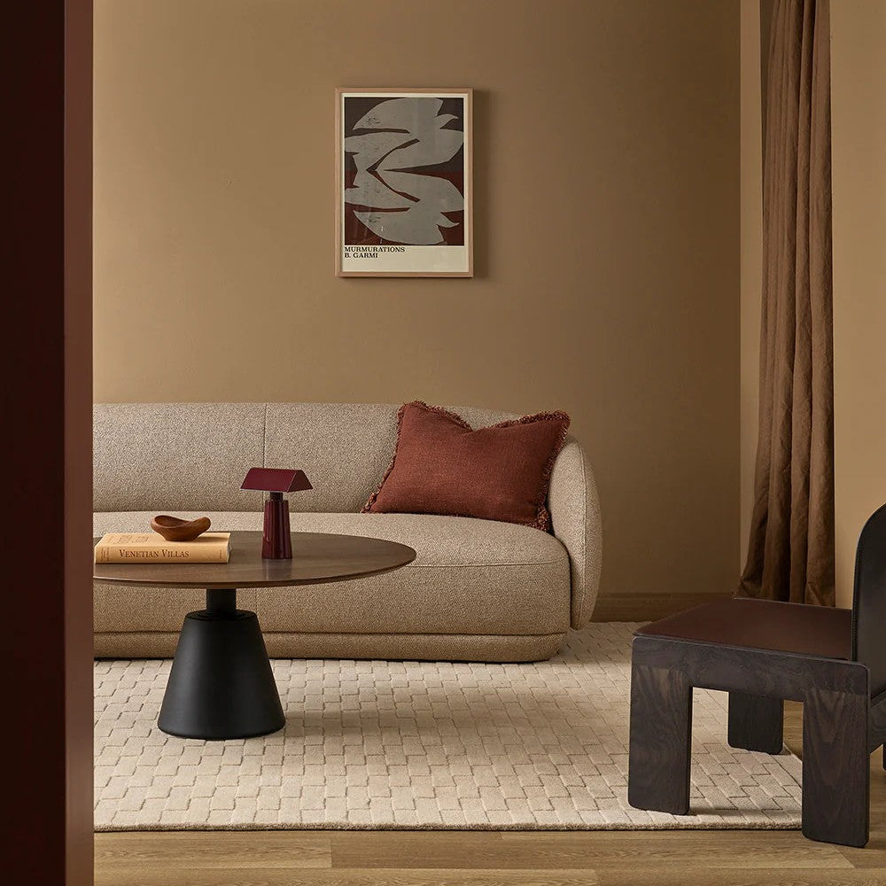 Modern living room with a beige sofa, round coffee table, almond floor rug and abstract art on the wall.