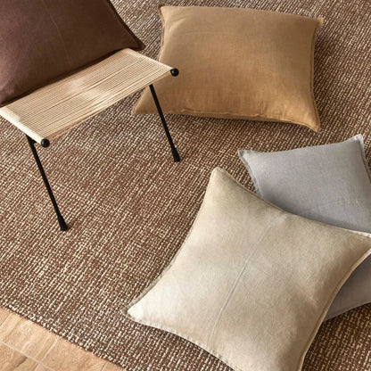 Decorative pillows on a textured rug with a chair in the background