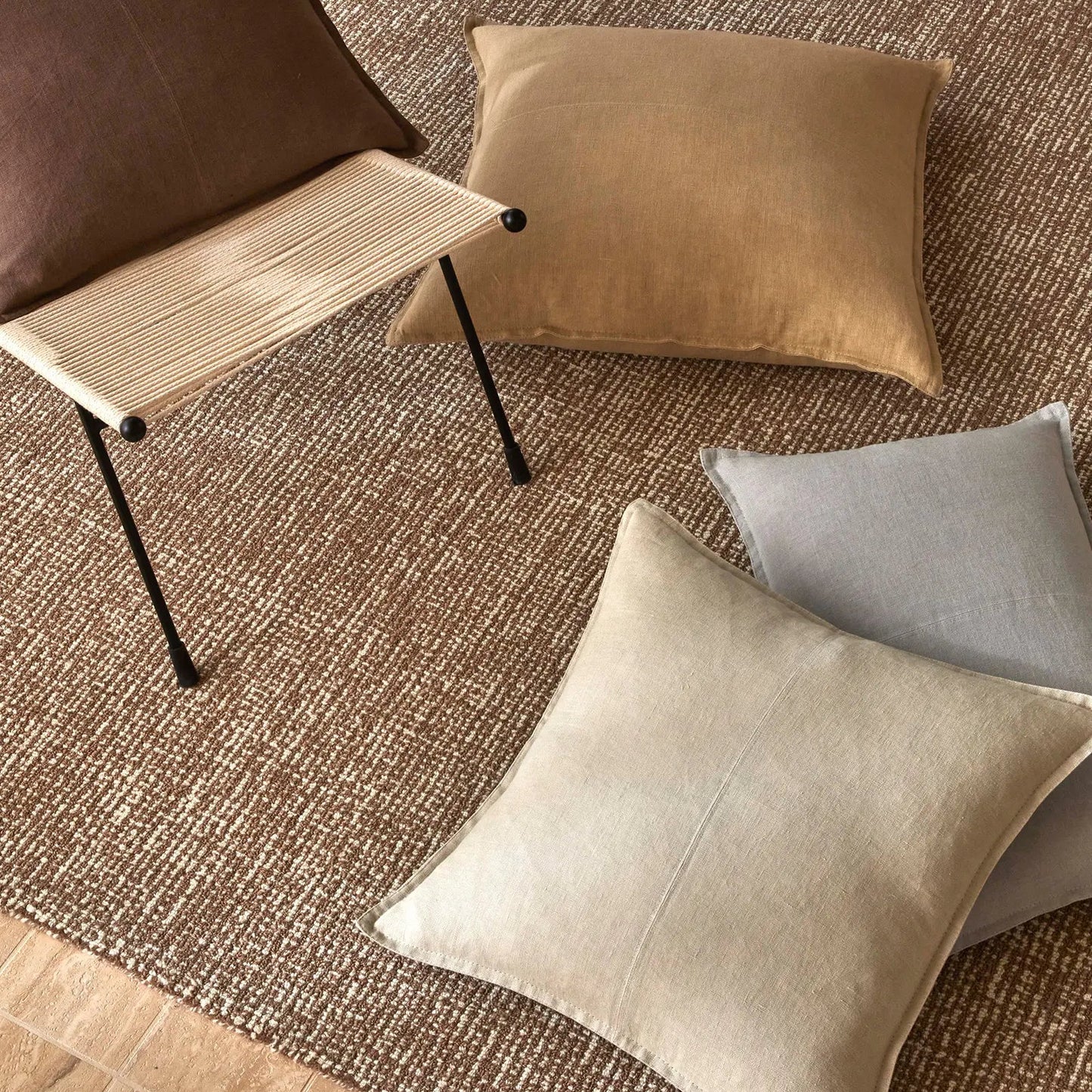 Decorative cushions on a textured rug with a chair in the background