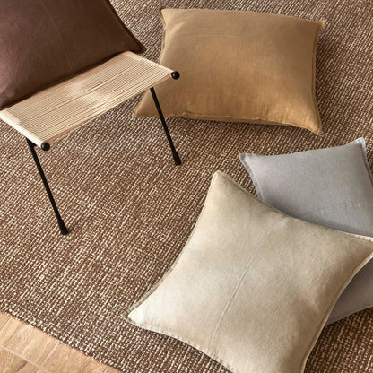 Decorative cushions on a textured rug with a chair in the background