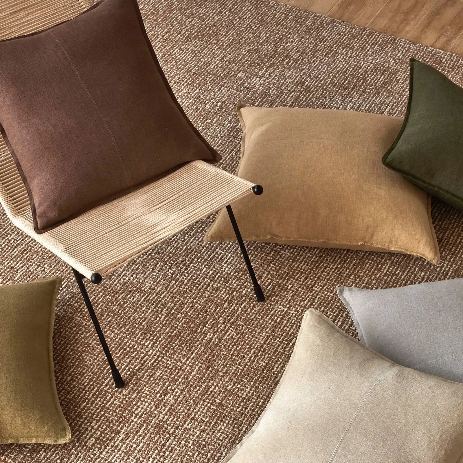 Chair with brown cushion on a textured floor with various pillows.