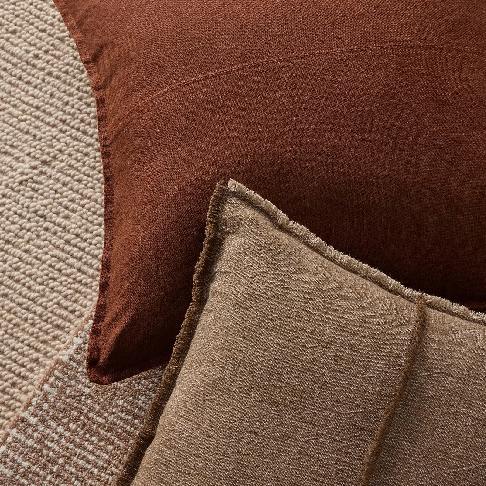 Close-up of two textured cushions, one brown and one beige, on a textured surface.