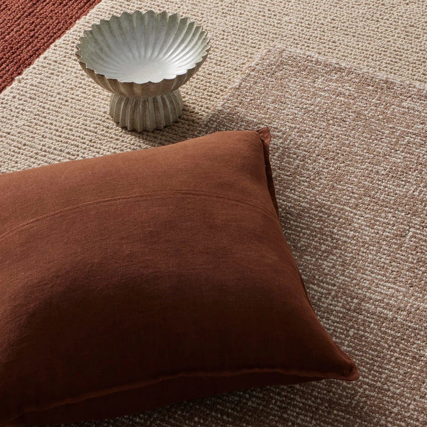 Brown cushion and decorative bowl on textured rugs