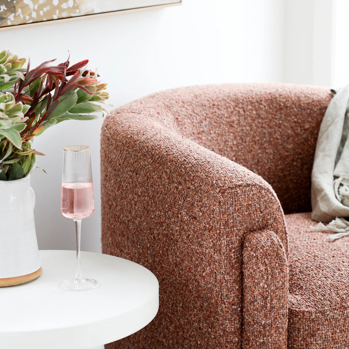 Blush textured armchair with a glass of pink drink and vase of flowers on a white side table.