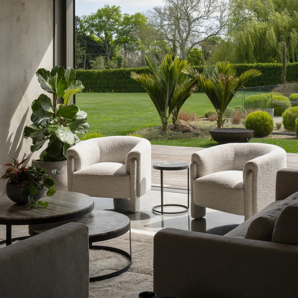 Modern living room with cream textured armchairs and a beige sofas, featuring a garden view.