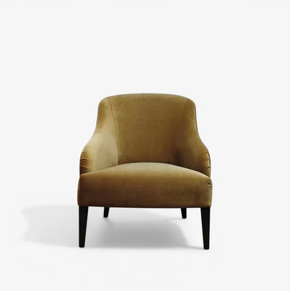 A single upholstered armchair in a warm gold/tan velvet fabric with dark tapered legs, photographed against a clean white studio background.