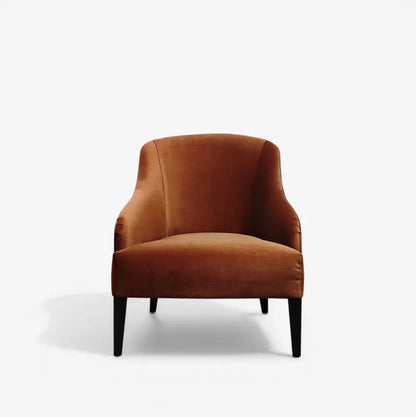 A modern accent chair upholstered in warm rust-brown velvet with tapered black legs, shown against a plain white studio background.