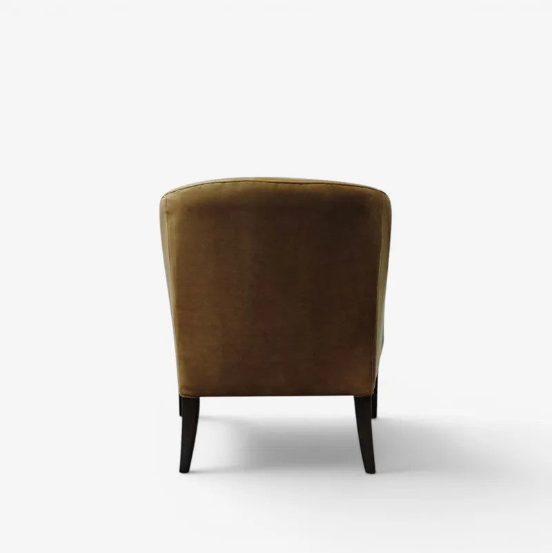 A single upholstered armchair shown from the back, featuring a warm gold/tan velvet fabric and dark tapered legs, set against a plain white studio background.