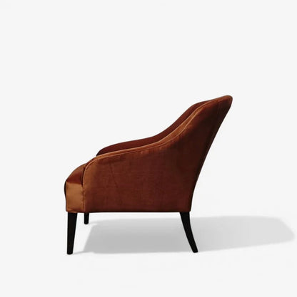 A single upholstered accent chair in a rich rust-brown velvet fabric, shown from a side profile view on a clean white background with a soft shadow.