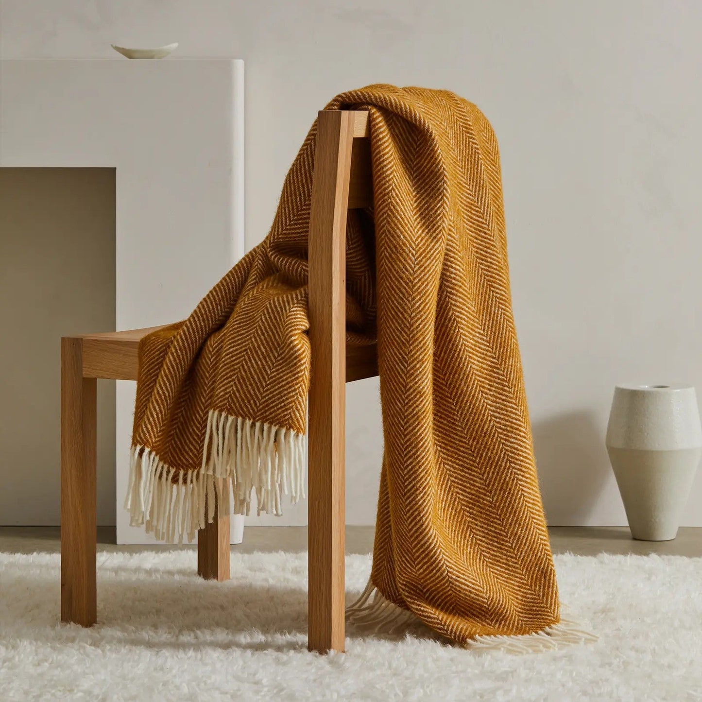 Amber textured blanket draped over a wooden chair in a minimalistic room.