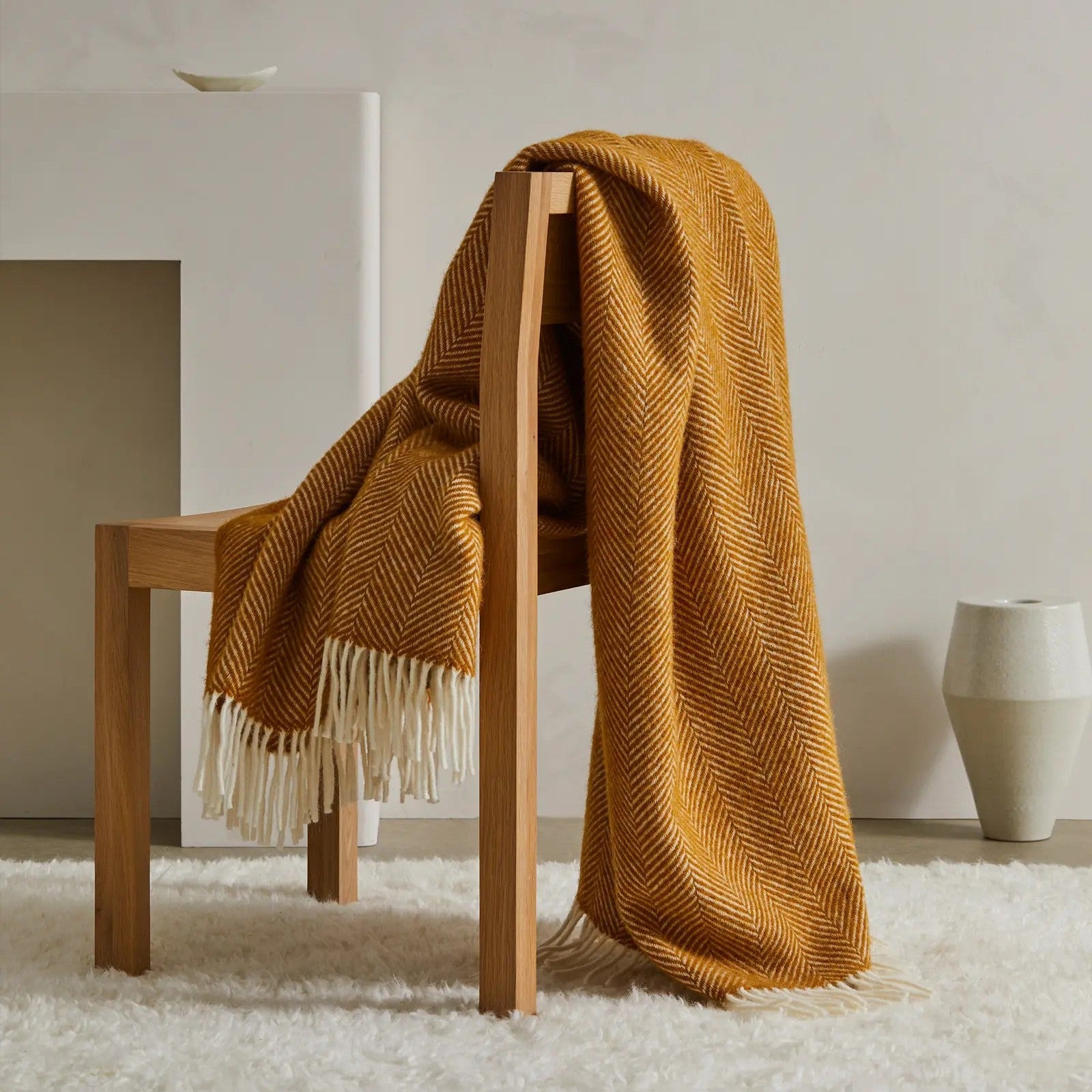 Amber textured blanket draped over a wooden chair in a minimalistic room.