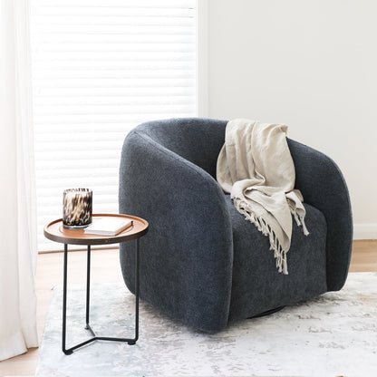 Steel blue armchair with a beige blanket in a room with a small round table and a candle.