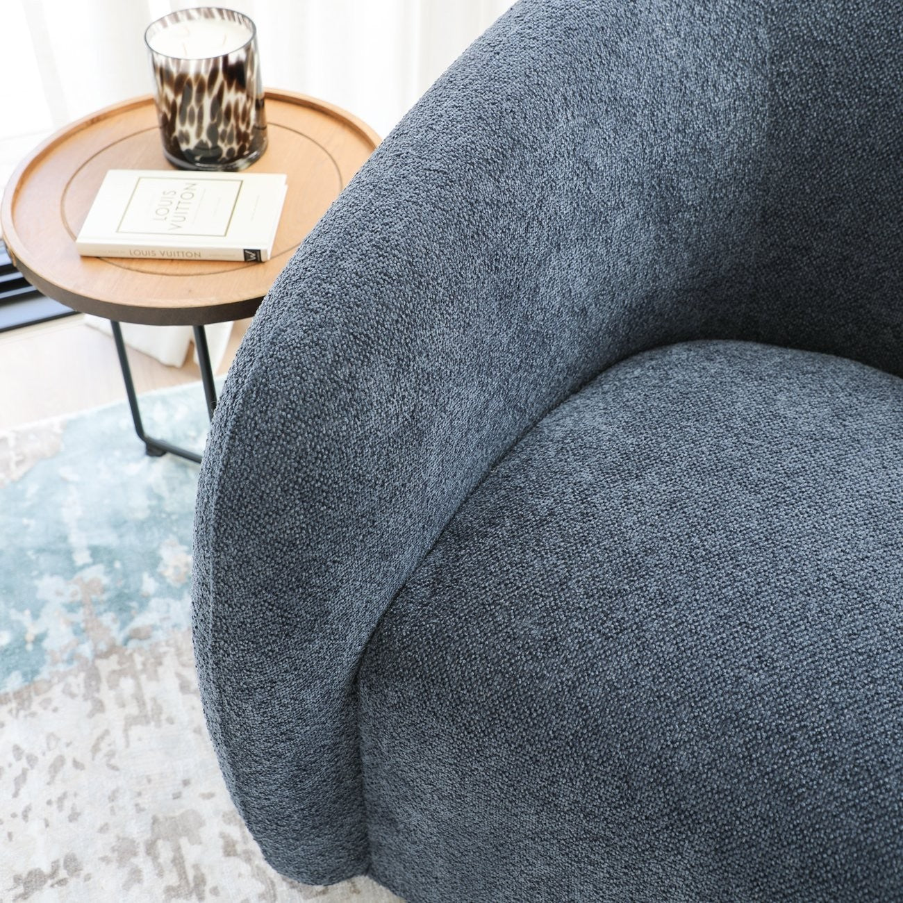 Close-up of a textured steel blue armchair with a small round table in the background.