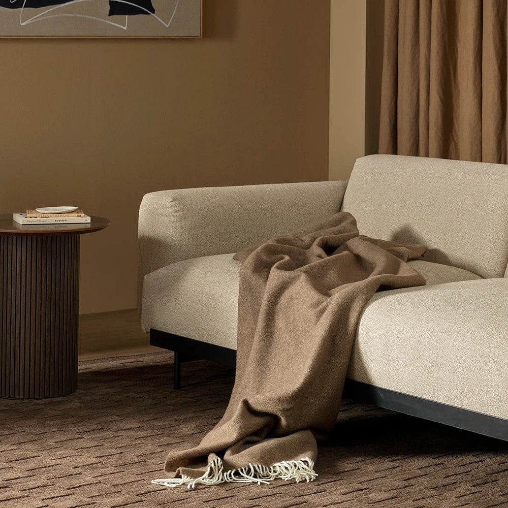 Beige sofa with a brown blanket draped over it in a room with abstract art and a side table.