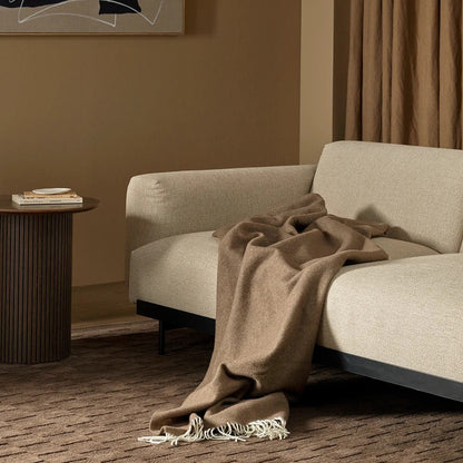 Beige sofa with a brown blanket draped over it in a room with abstract art and a side table.