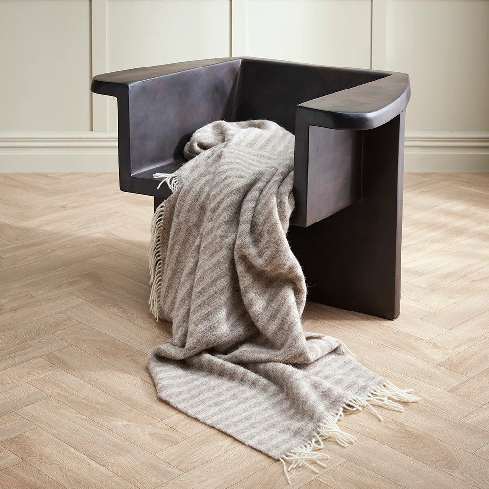Modern chair with a oatmeal blanket on a wooden floor and panelled wall background