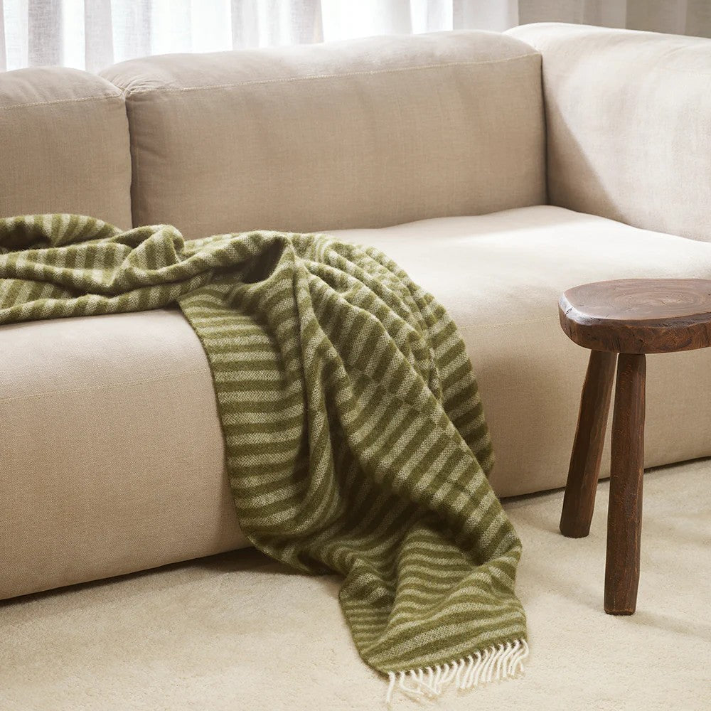 Beige sofa with a olive green striped throw blanket and a wooden side table in a living room setting.
