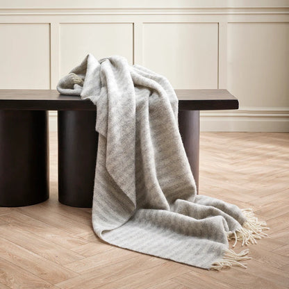 Silver Grey throw blanket draped over a black bench against a neutral wall.