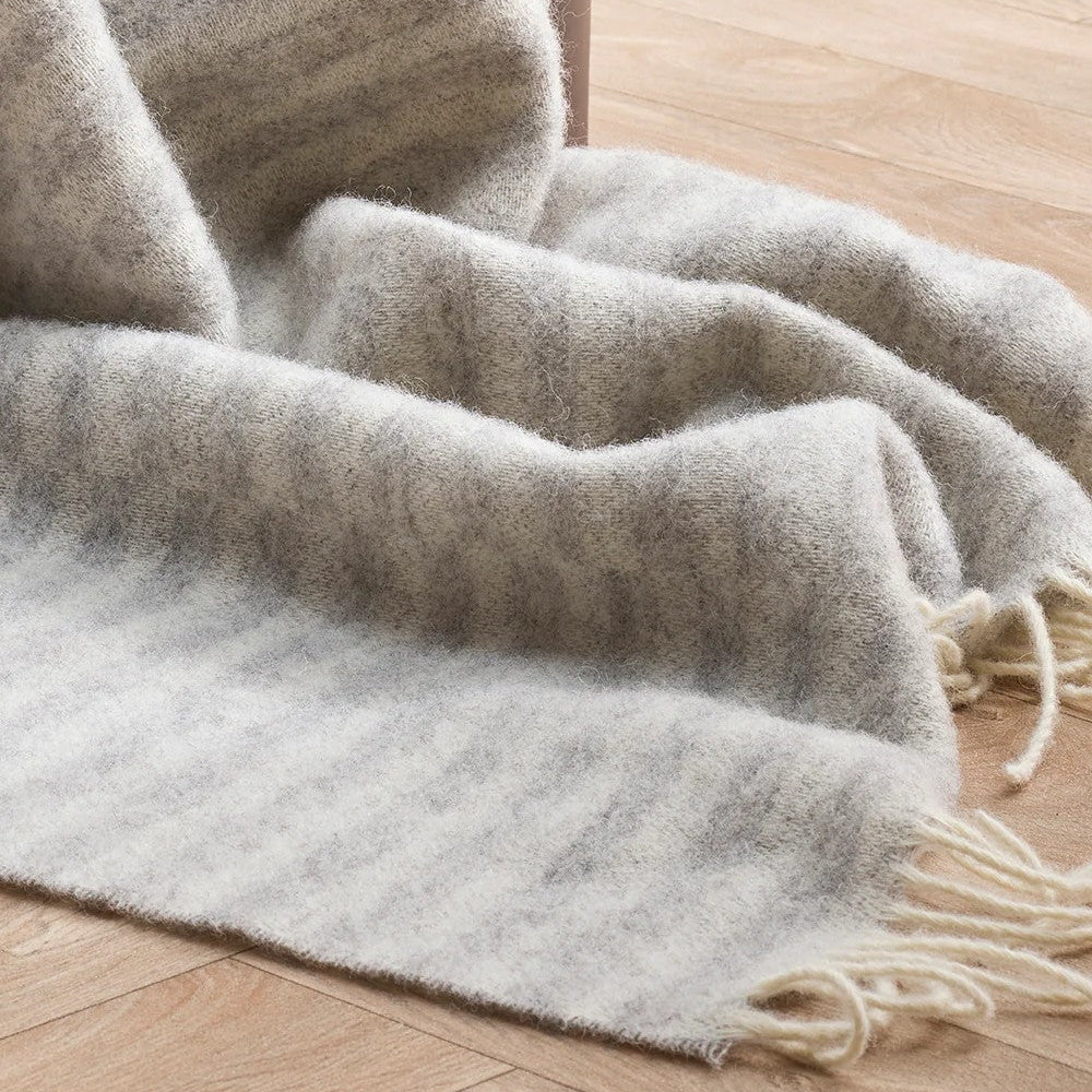 Silver Grey throw blanket with cream fringe on a wooden floor