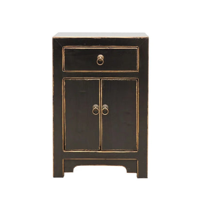 A small black bedside cabinet with two doors and a top drawer, featuring distressed natural trim and antique-style ring pulls, shown against a plain white background.