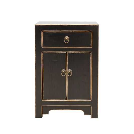 A small black bedside cabinet with two doors and a top drawer, featuring distressed natural trim and antique-style ring pulls, shown against a plain white background.