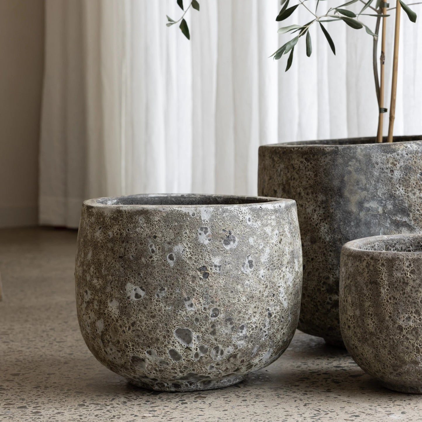 Three concrete planters of varying sizes on a neutral surface with a curtain in the background.
