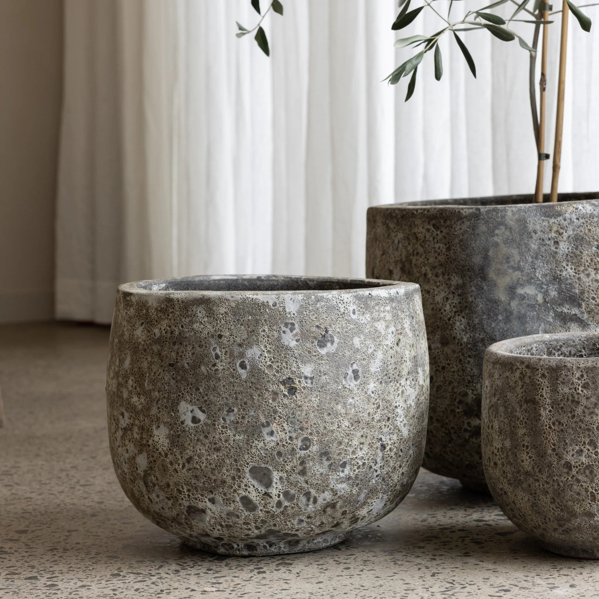 Three concrete planters of varying sizes on a neutral surface with a curtain in the background.