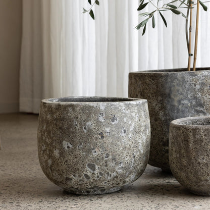 Three concrete planters of varying sizes on a neutral surface with a curtain in the background.